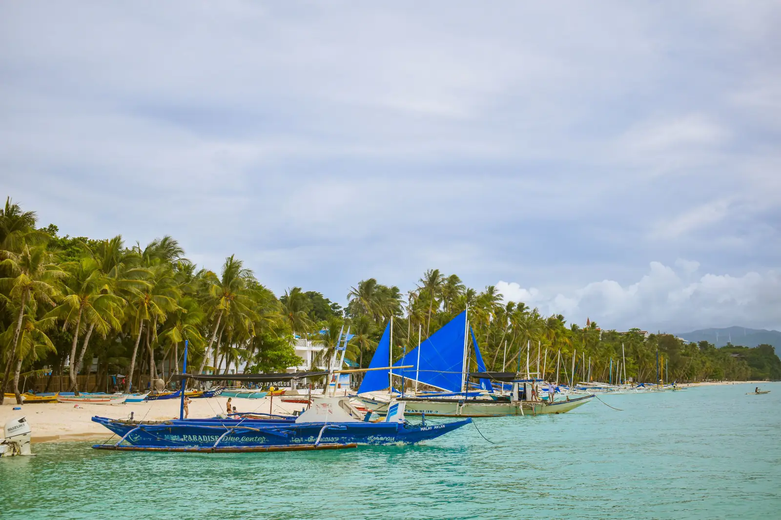 Tropical beach with blue sailboats and coconut trees in Boracay, Philippines.