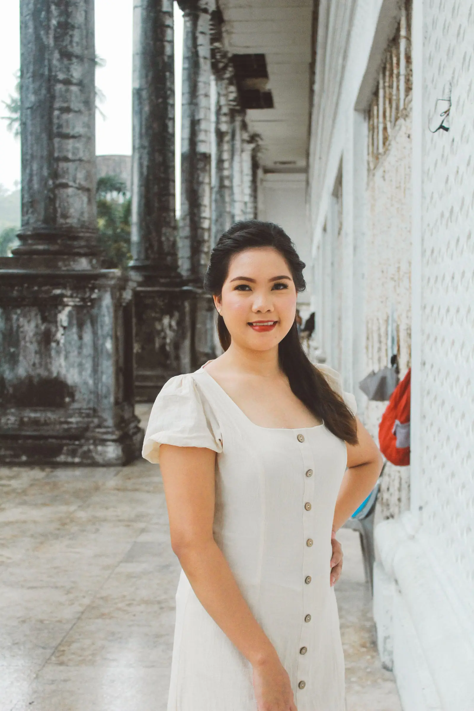 Woman in a white dress smiling by a historic building with columns.