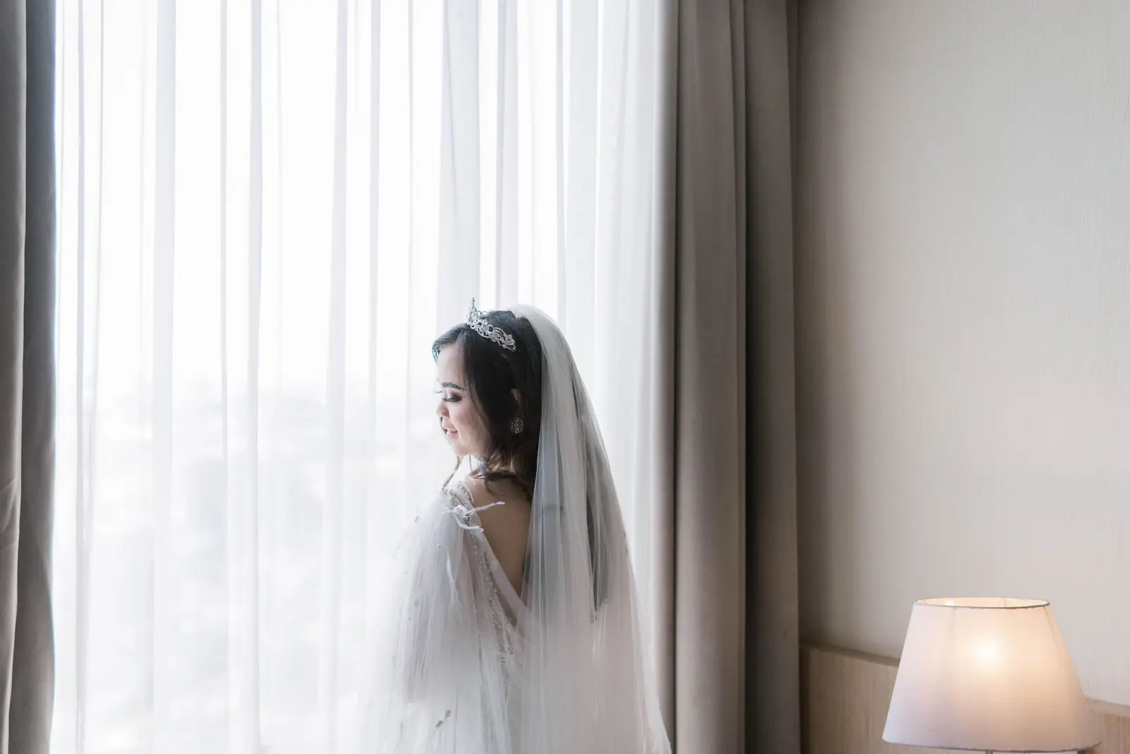 A bride standing by a sunlit window.