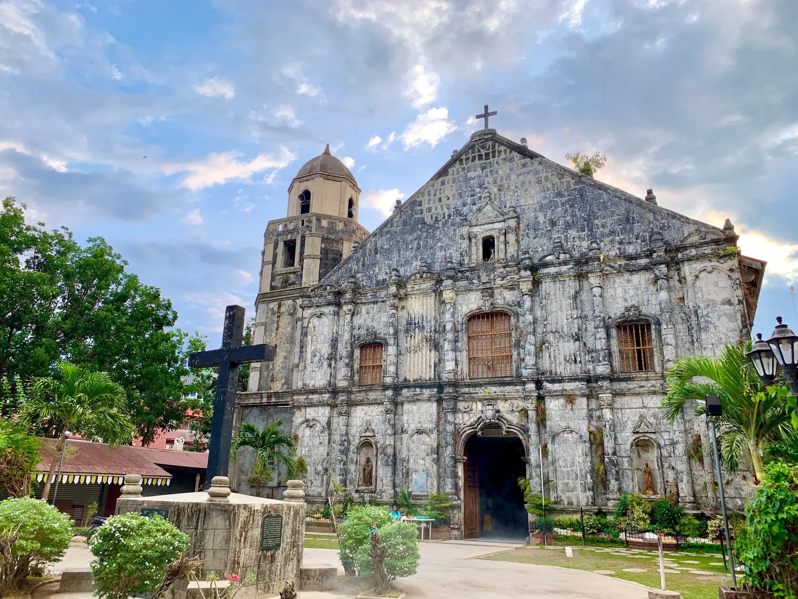 Baroque-style stone church in Bolinao, Philippines, amid greenery.