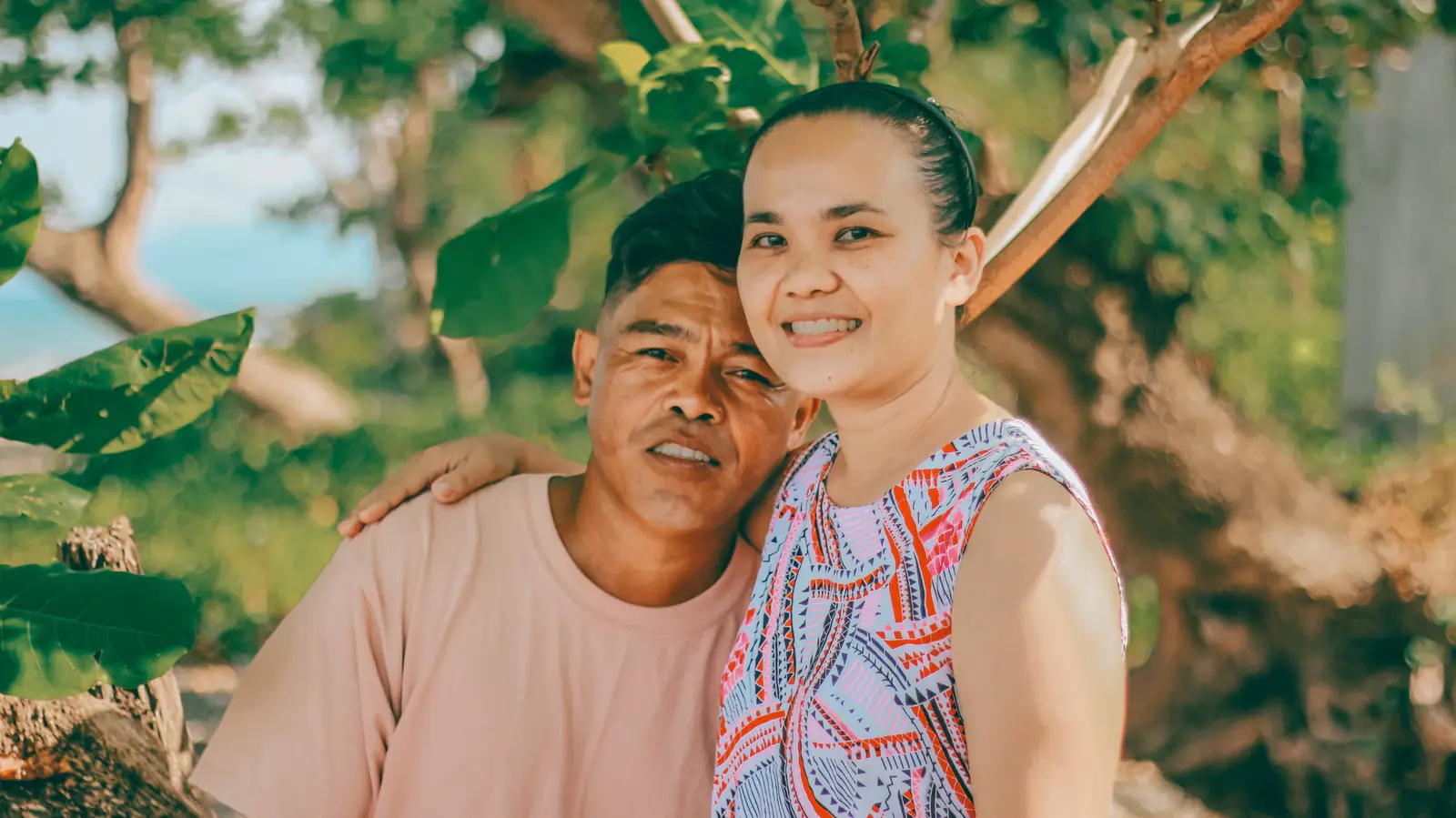 Smiling couple hugging on a sunny day in a lush forest.