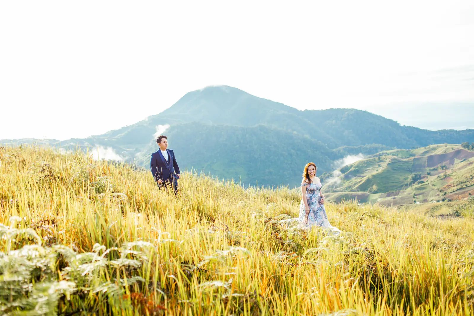 A couple in a field with mountains behind them.