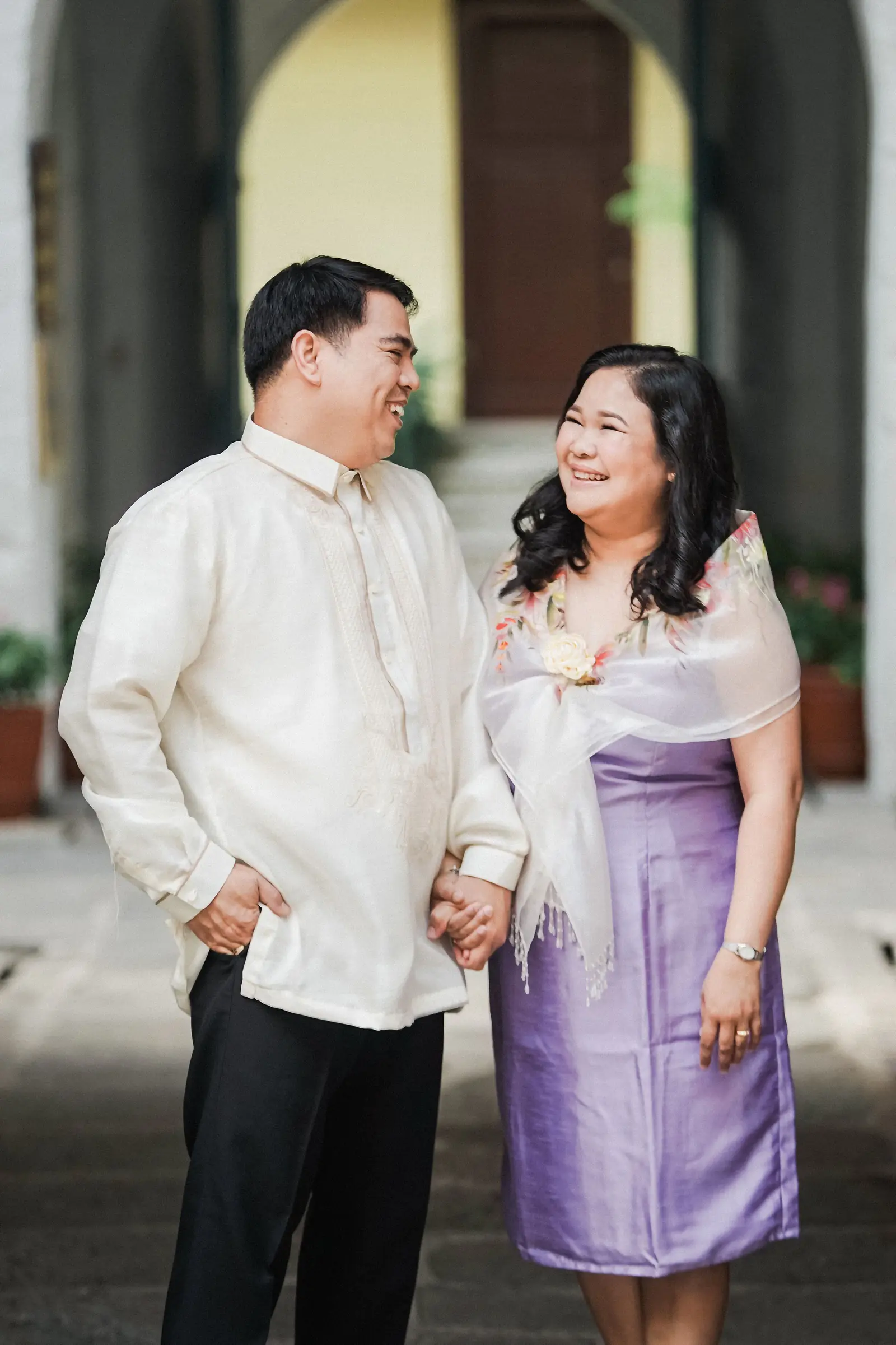 A couple in traditional Filipino attire holding hands and smiling.