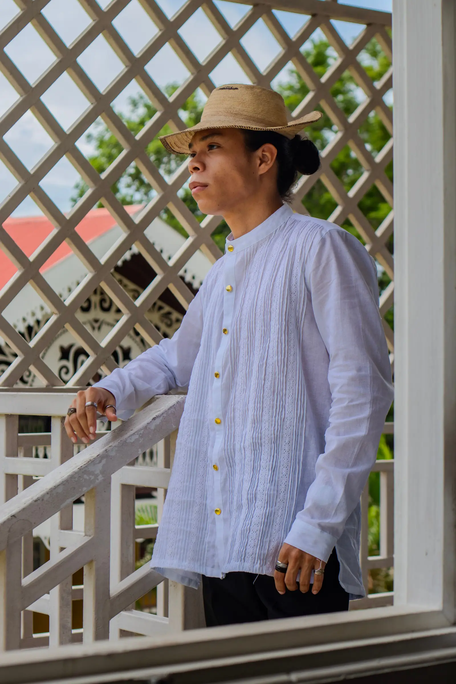A man in a white traditional shirt and straw hat on a decorated balcony.