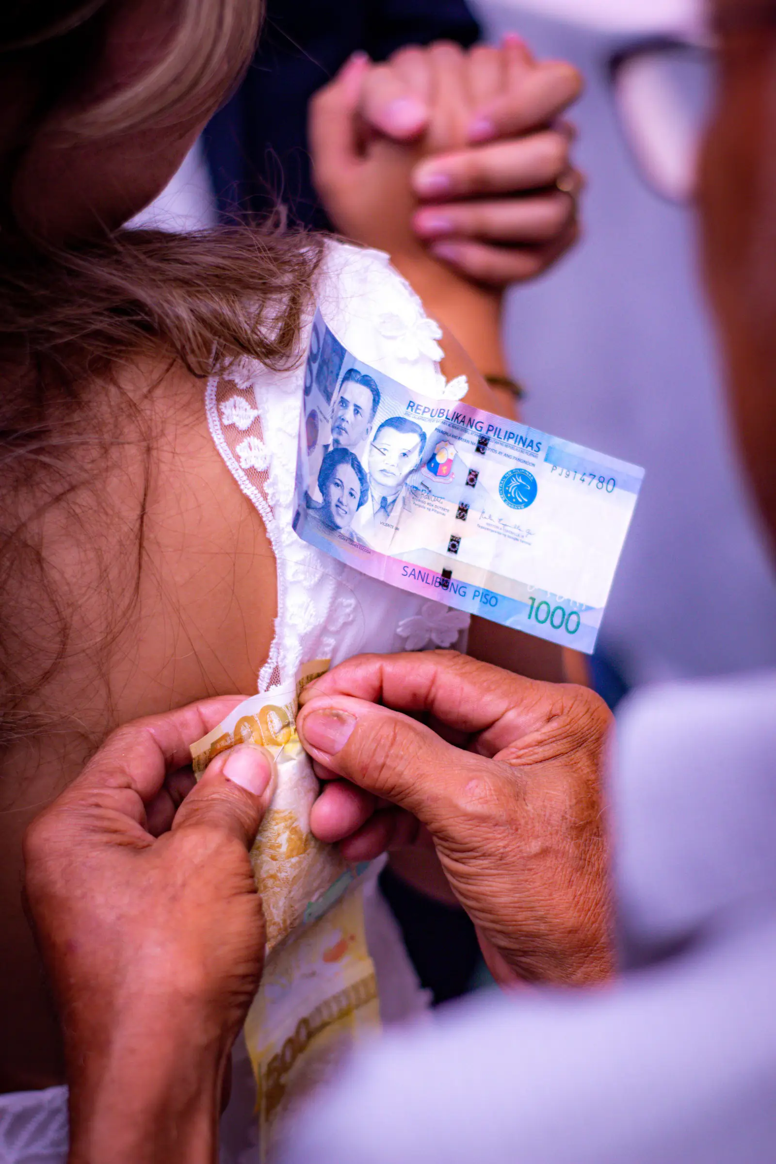 Hands pinning Philippine peso bills to clothes, a Filipino wedding tradition.